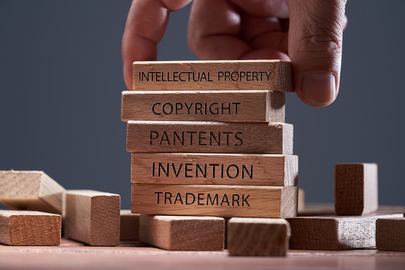 man adding a  block showing the words Intellectual property on top of  other wooden blocks