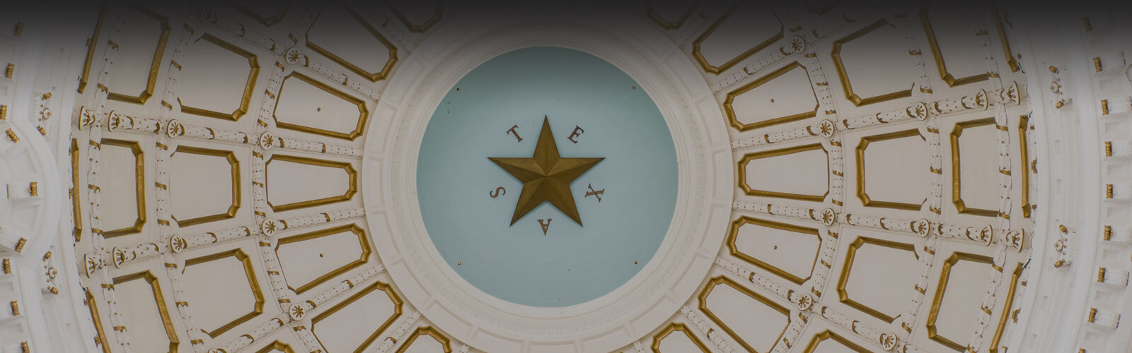 A view looking up at the ornate domed ceiling of the Texas State Capitol, featuring a large gold star in the center with the word
